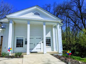 Universalist Unitarian Church of Farmington pictured in the spring with a blue sky and pinwheels in front