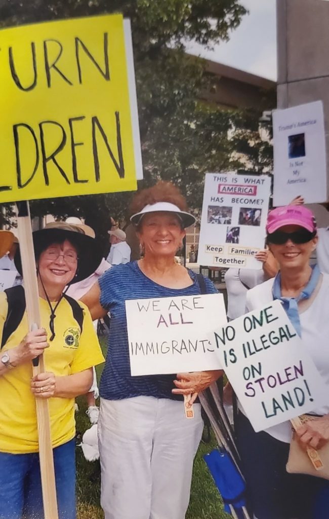 UUCF members pose for a group photo while marching for immigration rights. They hold signs saying "No one is illegal on stolen land" and "We are all immigrants".