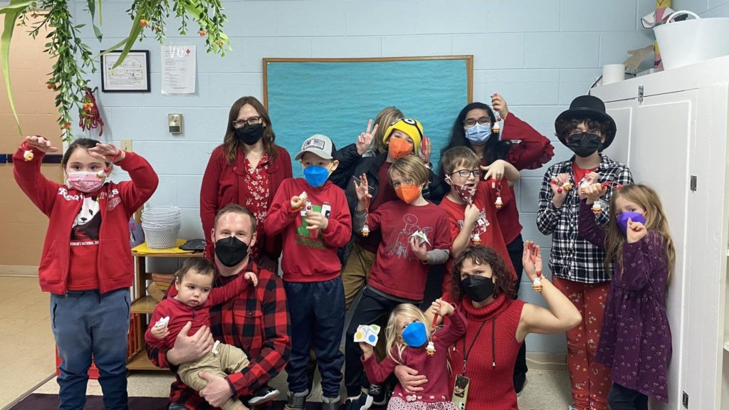 A group of children and adults, wearing red shirts, jackets, and pants, show off small keychain charms celebrating the Chinese New Year