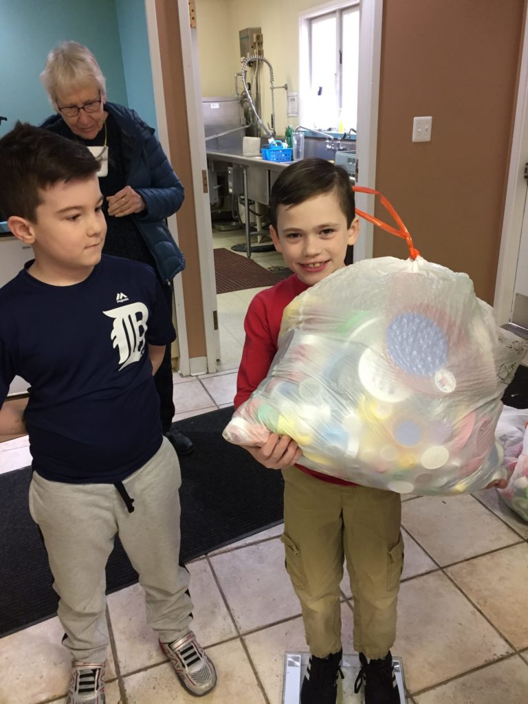 A child holds a garbage bag stuffed with bottle caps collected to build recycled plastic benches