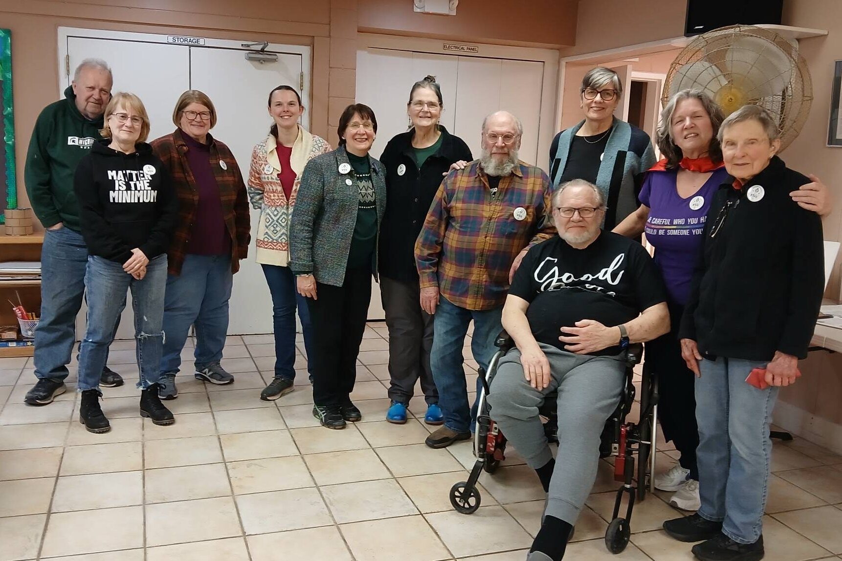 A group of men and women pose for a group photo. They are all wearing white circular pins celebrating their achievements