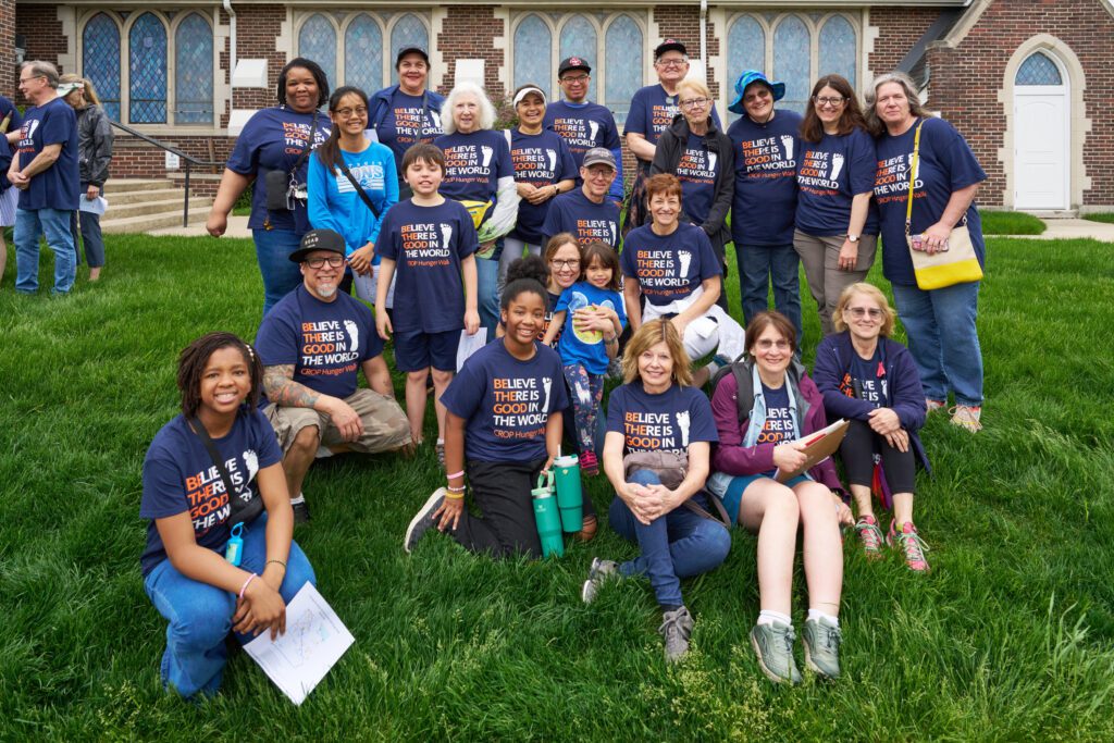 A group of approximately 20 people of various ages and genders pose together for a photo on a grassy lawn.