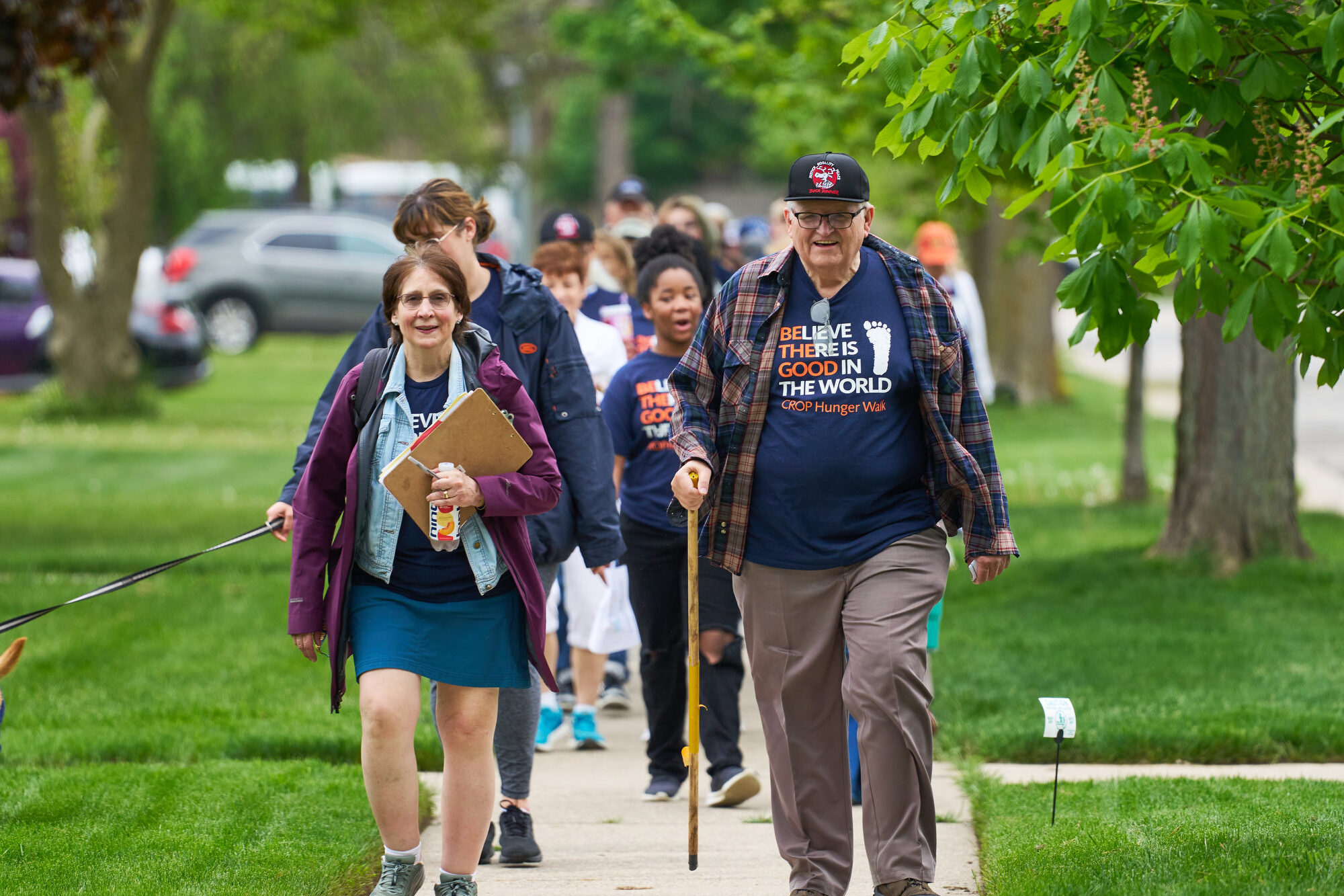 A woman and a man walk side by side down a sidewalk. They are walking toward the camera and smiling.